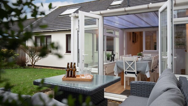 A modern house with a glass-enclosed patio, a dining area with a table and chairs, and a garden. - Kittiwake - Short Walk to Beach and Village (Saundersfoot)