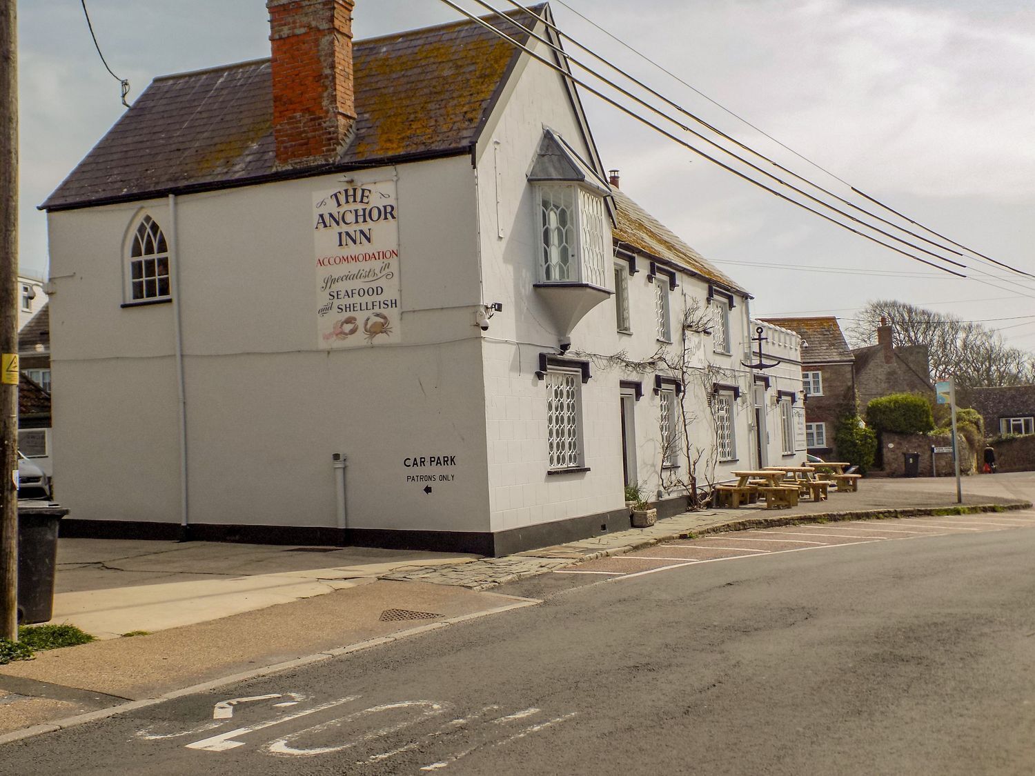 A white building with a sign advertising The Anchor Inn, a car park, and outdoor seating.