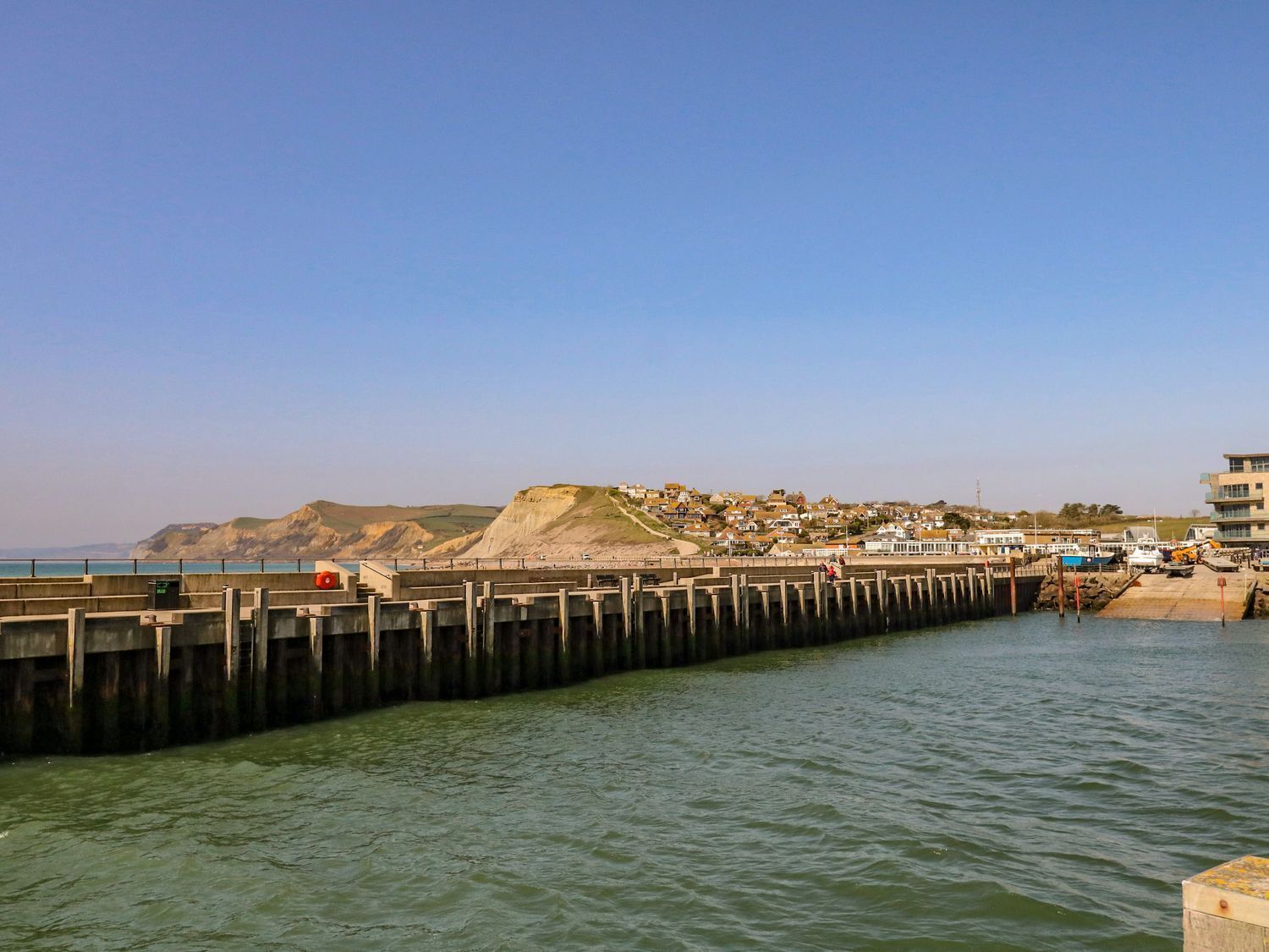 Une jetée côtière d’où l’on peut admirer une ville et des falaises en arrière-plan.