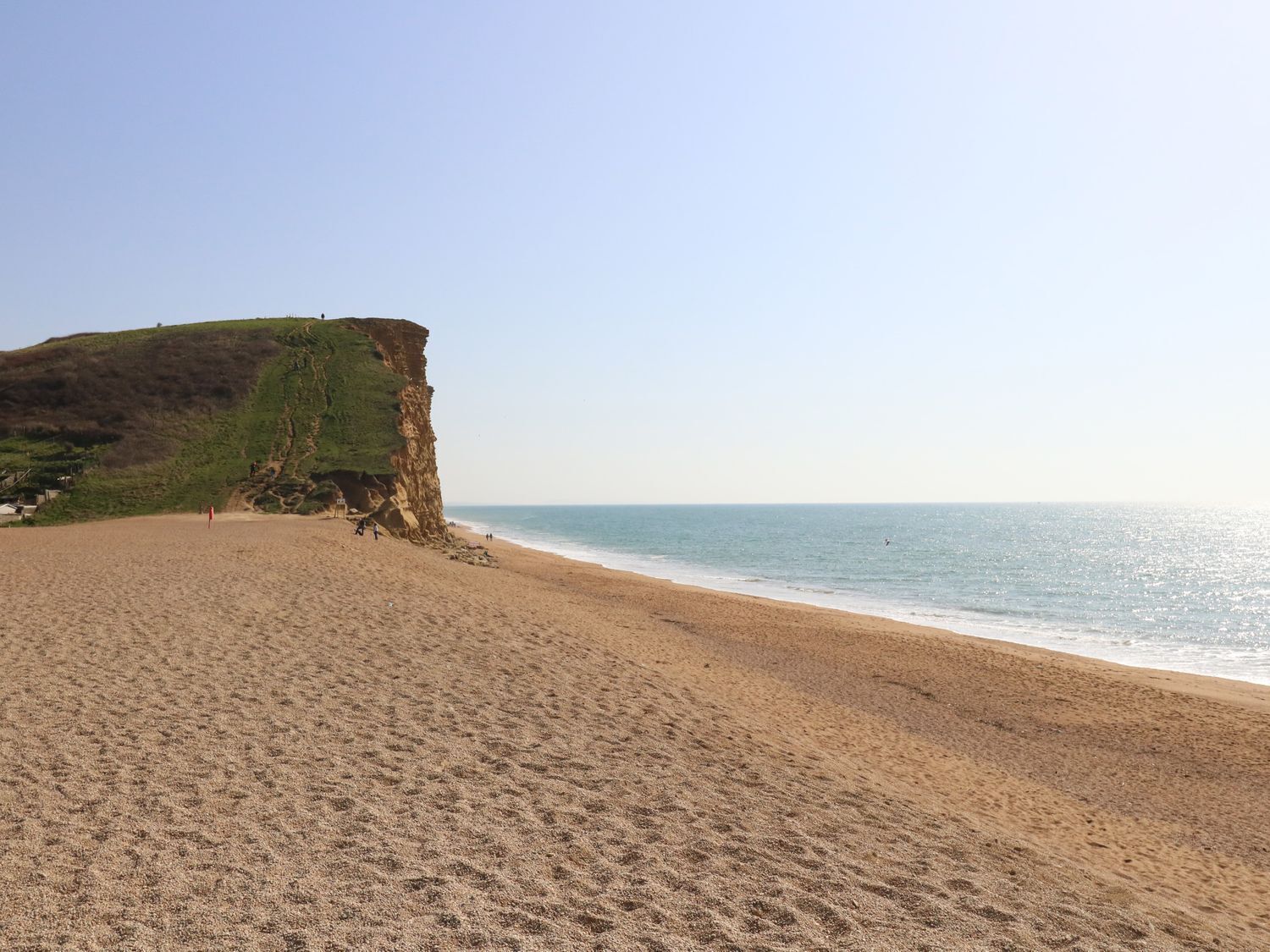 Une plage avec une grande falaise, un rivage sablonneux et un ciel dégagé.