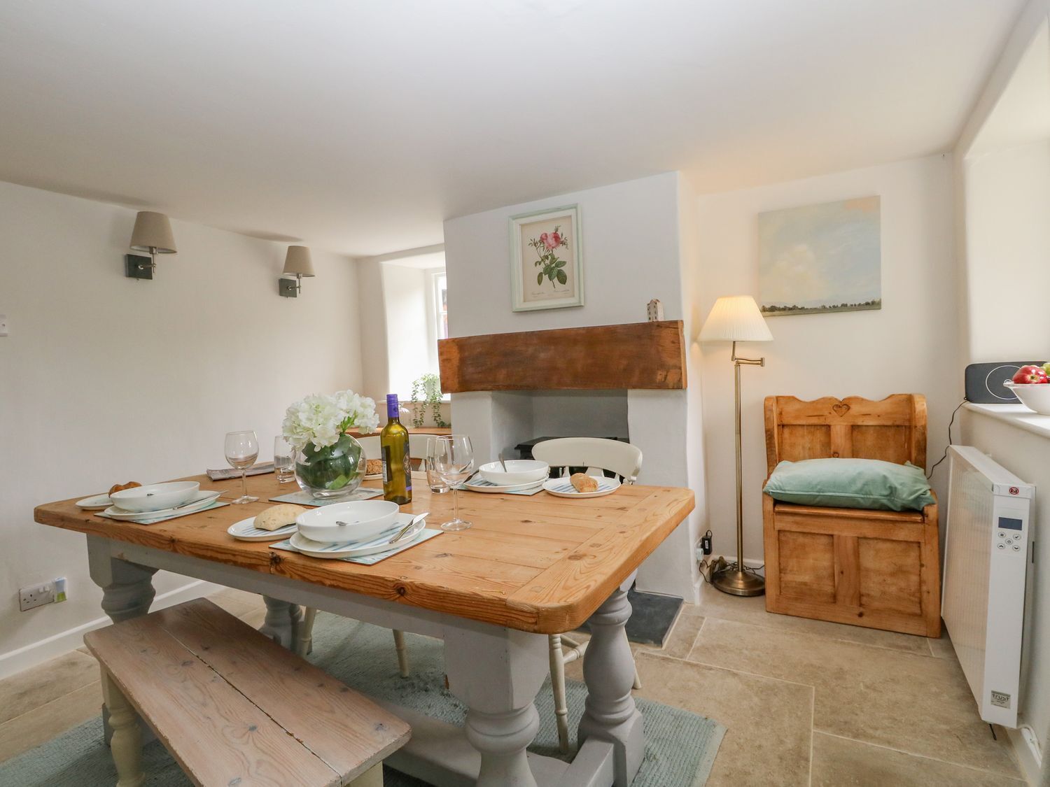 Un comedor con una mesa de madera dispuesta para dos personas, un banco y un pequeño armario de madera con cojín verde.