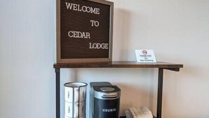 Cedar Lodge -hotellin sisäänkäynnin yläpuolella on tervetulotoivotus, pöydällä on Keurig-kahvinkeitin ja pyyhe.