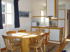 Un comedor con mesa y sillas de madera, una cocina con microondas y lavabo, y una ventana con cortinas.