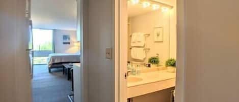 A narrow hallway leading to a bathroom with a sink and mirror. A bed is visible in the adjacent room.