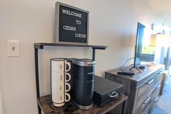 A reception desk with a welcome sign, a coffee machine, and a set of mugs. - Cute Cedar Lodge Studio with Balcony & Lake Views! (Laconia)
