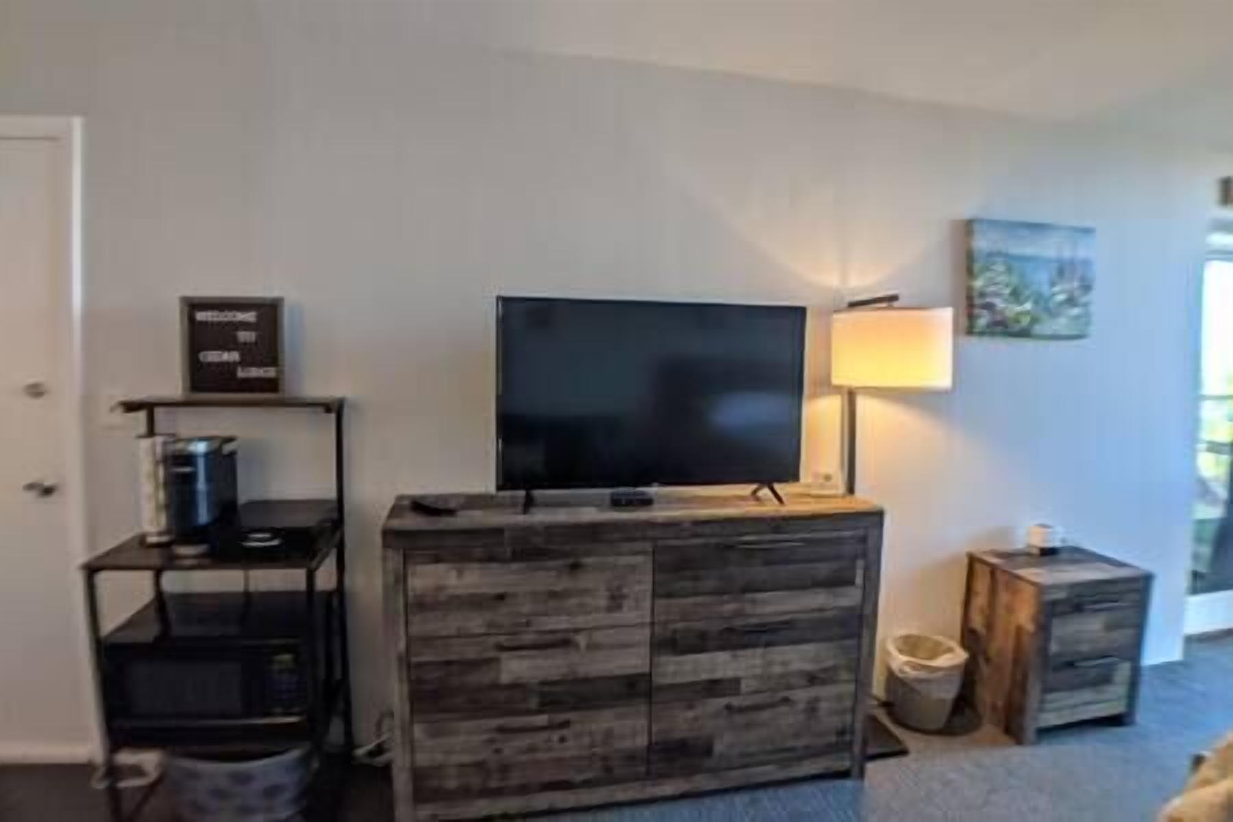 Una sala de estar con televisor de pantalla plana sobre un mueble de madera, una cafetera y una lámpara.