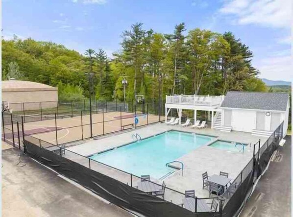 Ein Schwimmbad mit Basketballplatz, Liegestühlen und einer überdachten Sitzgelegenheit.