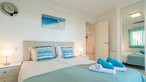 Habitación de hotel con una cama grande, dos mesitas de noche con lámparas, un cuadro con una playa y un espejo con una toalla sobre la cama.