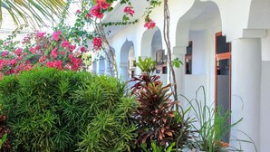 Un espace extérieur abrité, agrémenté d’arches blanches, d’une végétation luxuriante et de fleurs roses.