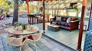 Un espacio al aire libre cubierto con una pérgola de madera, una mesa redonda con sillas y un sofá.