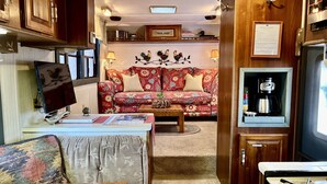 Interior compacto de autocaravana con kitchenette, sofá, mesa de comedor y cafetera pequeña.