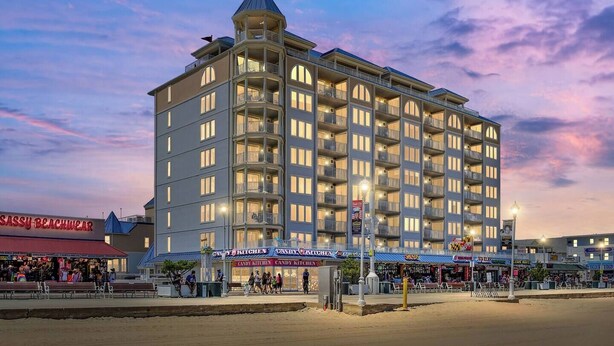 Un hôtel à plusieurs étages, doté d’une tourelle d’angle remarquable, de nombreux balcons et d’un espace commercial au rez-de-chaussée comprenant des boutiques.