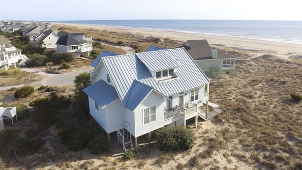 Ein Küstenhaus mit Metalldach, umgeben von Dünen und einem Strand.