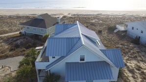 Ein Küstenhaus mit Metalldach, einer kleinen Veranda und Blick auf Strand und Meer.
