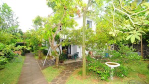 A garden pathway leading to a white building with a stone wall and a small patio area with chairs.