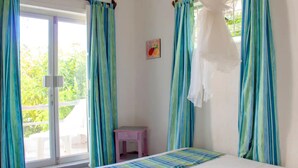 A bedroom with a bed, a small pink nightstand, and a window with curtains.