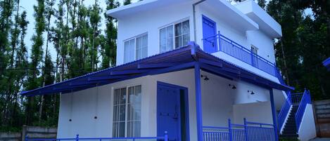 Un edificio de dos pisos con fachada blanca y detalles azules, que incluye un balcón y barandillas.