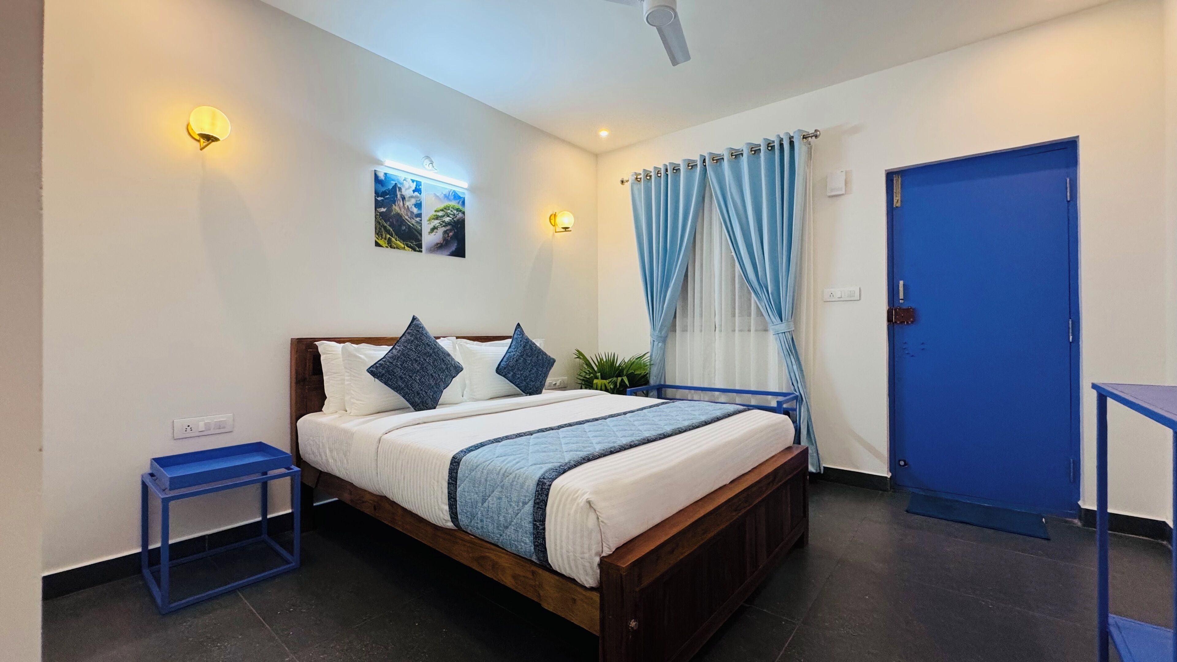 Ein Schlafzimmer mit einem hölzernen Bett, einem Nachttisch, einer blauen Tür und einer Wandleuchte.