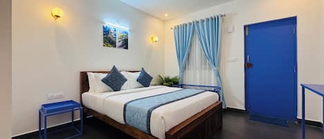 A bedroom with a wooden bed, a nightstand, a blue door, and a wall-mounted light fixture.