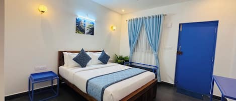 Un dormitorio ordenado con cama, mesitas de noche, una puerta azul y un ventilador de techo.