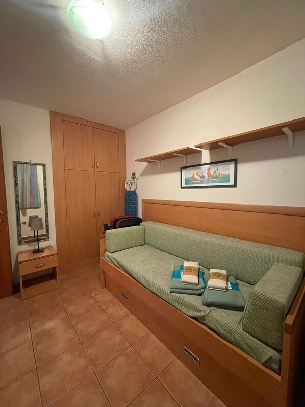 Ein kleiner, gemütlicher Raum mit einem grünen Sofa, einem Holzschrank, einem Tisch mit Lampe und einem Regal mit einem gerahmten Bild.