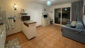 A compact living space with a kitchenette, a sofa, a dining area, and a sliding glass door leading to an outdoor area. - Appartement VUE MER Dans Résidence Standing Avec Piscine (San-Nicolao)
