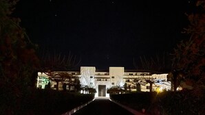 A nighttime view of a hotel with a central entrance, flanked by trees and illuminated pathways. - Appartement VUE MER Dans Résidence Standing Avec Piscine (San-Nicolao)