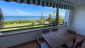 A balcony with a wooden table and chairs, overlooking a well-maintained garden and the sea. - Appartement VUE MER Dans Résidence Standing Avec Piscine (San-Nicolao)