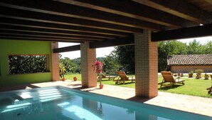 An outdoor swimming pool with a wooden pergola overhead, surrounded by potted plants and lounge chairs.