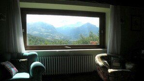 A room with a large window offering a view of mountains and greenery. There are two chairs and a radiator.