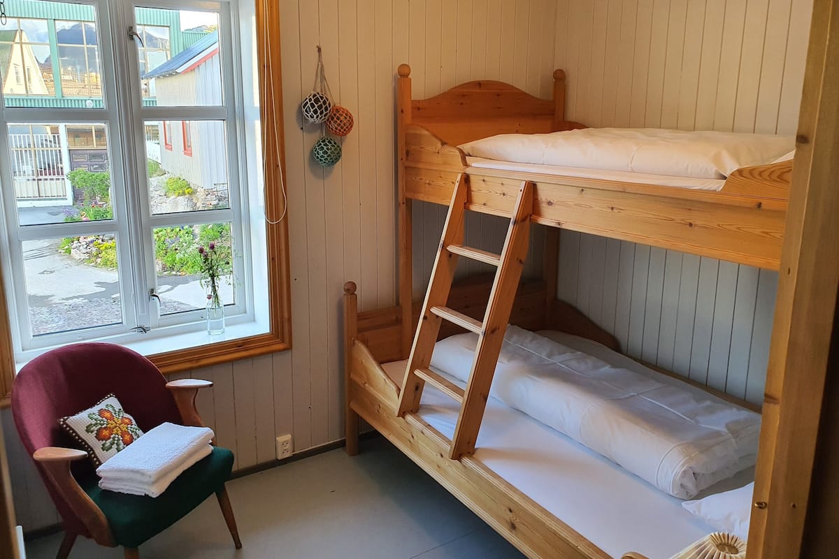 A bunk bed room with a window, a chair, and a small table.