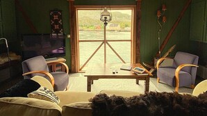 A cozy living room with a wooden ceiling, a large window, a television, and comfortable seating.