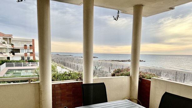 Un balcone con tavolo e sedie, affacciato su una spiaggia e una piscina.