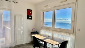 Una stanza con un tavolo di legno e due sedie nere, una finestra con vista sul mare e una porta con tenda.