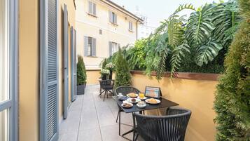 Un patio con mesa lista para el desayuno, rodeado de plantas en macetas y vistas a la ciudad.