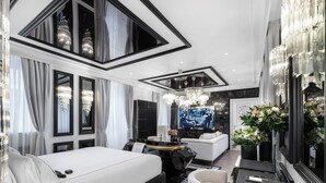 Une chambre d’hôtel moderne dotée d’un grand lit, d’un coin salon avec un canapé et une petite table, d’une télévision et d’un miroir orné de motifs floraux.