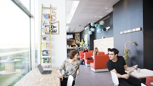 A modern interior with a wooden table, a laptop, and a person reading a magazine. - Résidence Kley Toulouse (Toulouse)