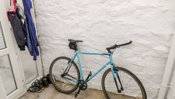 Een blauwe fiets staat tegen een witte muur in een hoek, met een schoenenrek met verschillende schoenen en jassen.