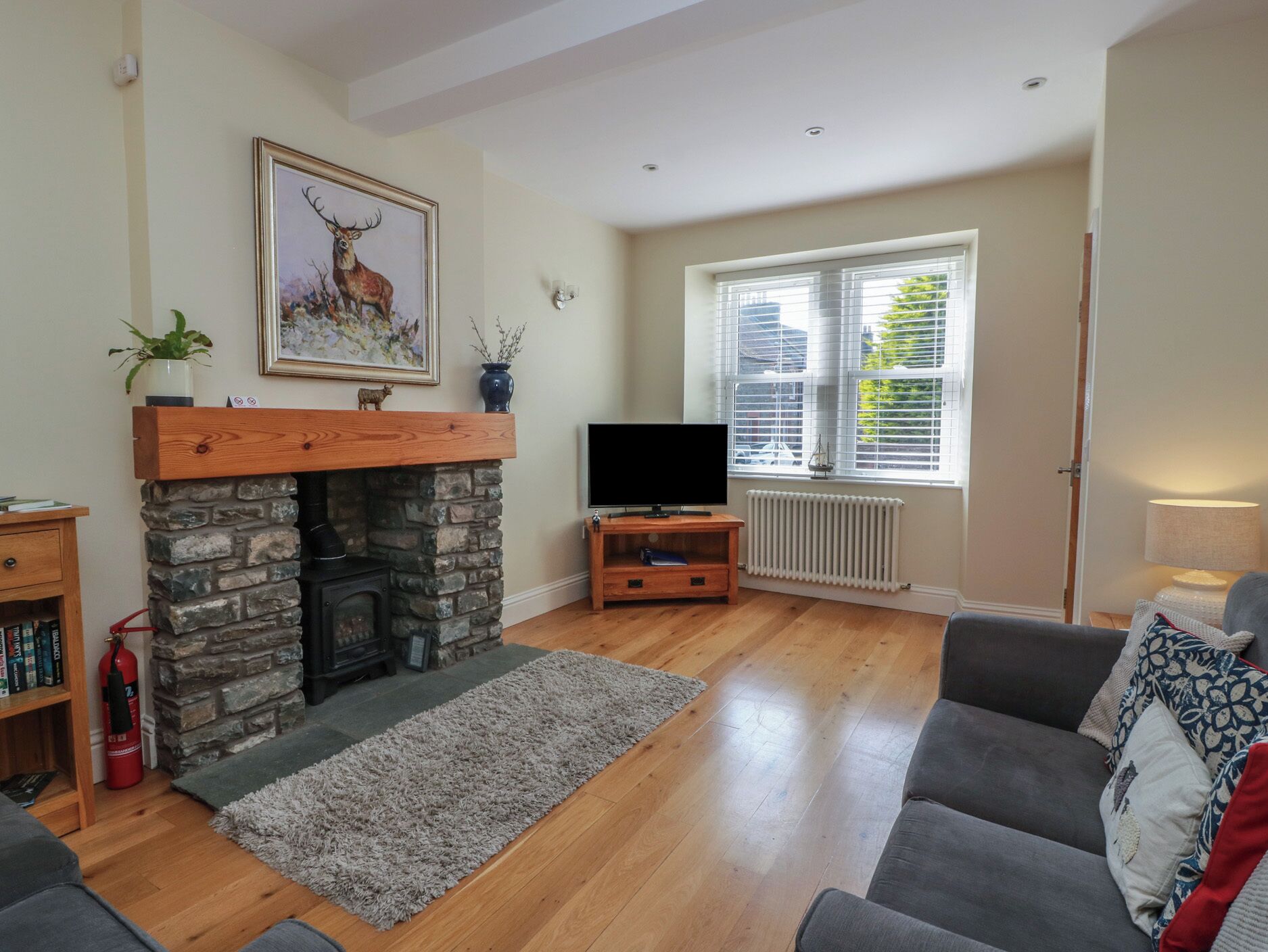 A living room with a stone fireplace, a television on a wooden stand, a sofa, and a window with blinds.