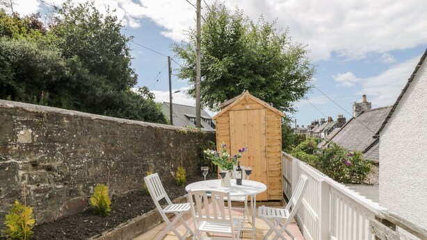 Eine Terrasse mit einem Holzschuppen, weißen Stühlen und einem Tisch mit Weingläsern und Blumen.