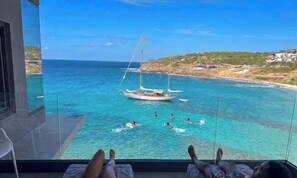 Un balcone con vista sul mare, una barca a vela e persone che nuotano.