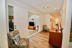 A hallway with a wooden floor, a door leading to a living room, and a reception desk with a cat on it.