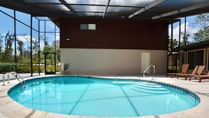 Une piscine avec une terrasse carrelée, un espace couvert doté d’une porte et une vue sur les arbres à travers de grandes fenêtres.