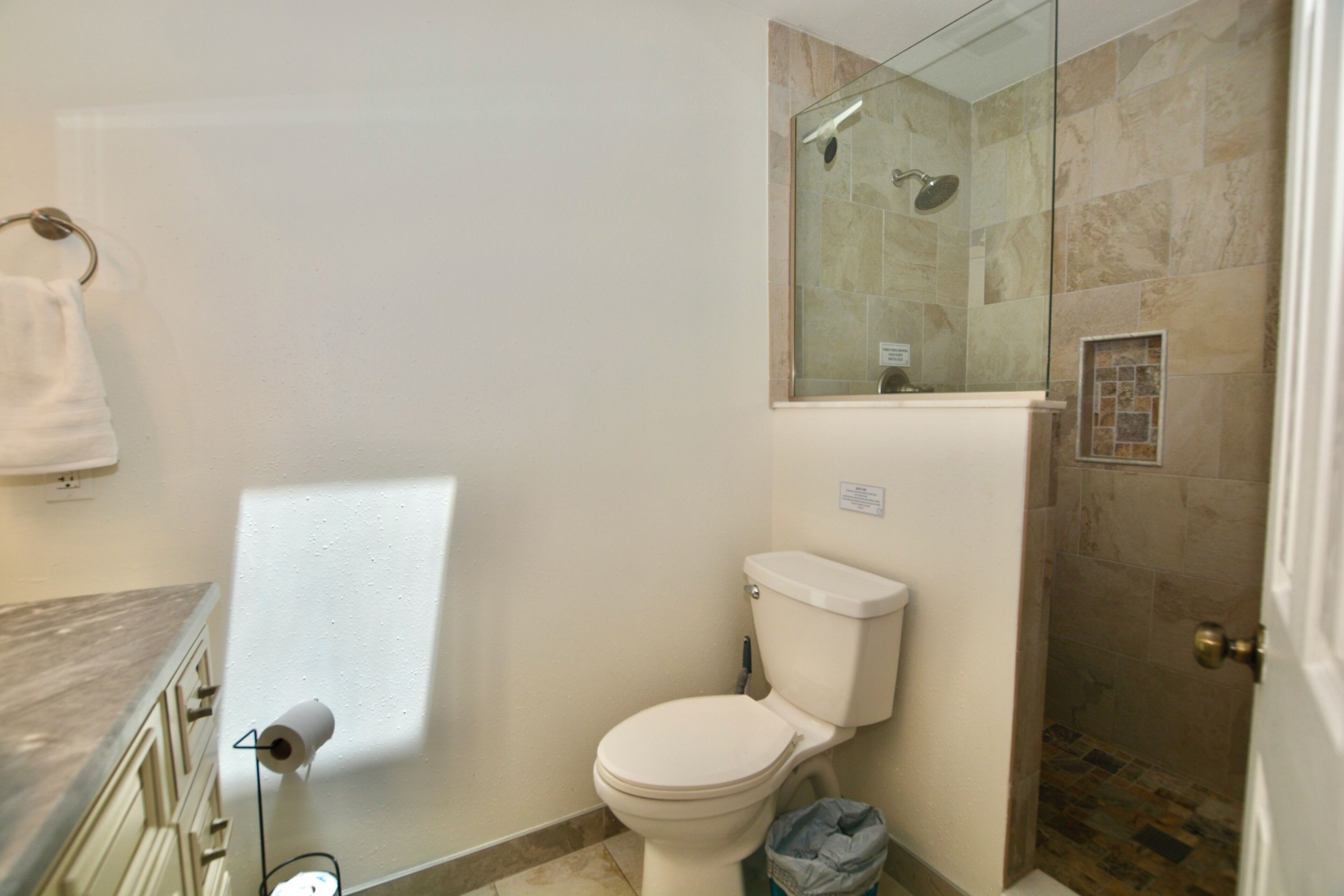 A bathroom with a toilet, a glass shower enclosure, and a marble countertop.