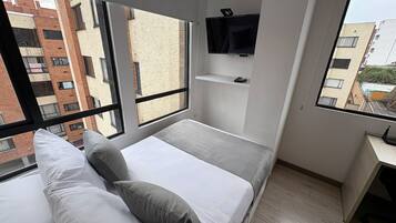 A modern bedroom with a bed, pillows, a TV, and a desk.