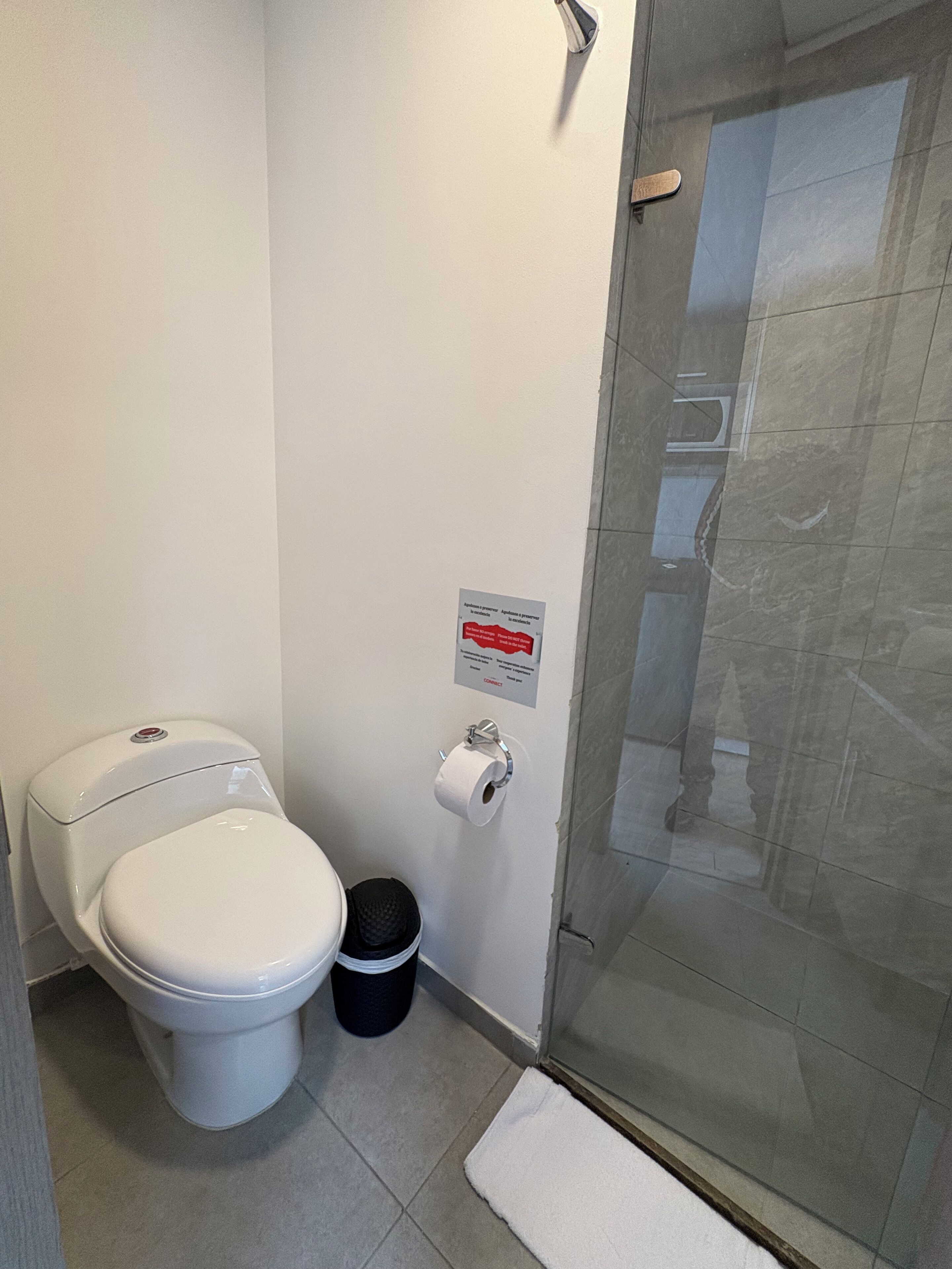 Un baño con inodoro, un cubo de basura, dispensador de toallas de papel y cabina de ducha de vidrio.
