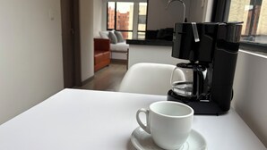 Una taza blanca sobre un plato en una mesa, con una cafetera al fondo.