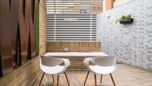 Un área de estar moderna al aire libre con un banco y dos sillas, piso de madera y una pared de ladrillo con jardinera.