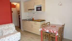 A compact kitchen with wooden cabinets, a built-in microwave, and a small dining area with a table and chairs. - Sea and shops on foot, T2 ground floor for 4 people. (DAMGAN)