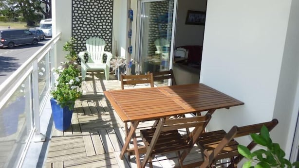 Un balcón con una mesa y sillas de madera, una planta en maceta y un muro decorativo.